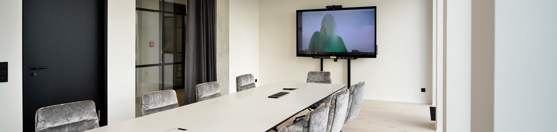 Moderner Besprechungsraum mit großen Konferenztisch, grauen Samtstühlen und einem Smartboard