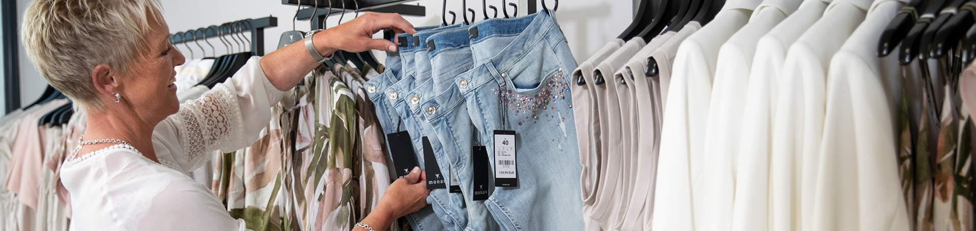 Eine Mitarbeiterin hängt eine Hose auf eine Kleiderstange die bereits mit vielen Artikel behangen ist